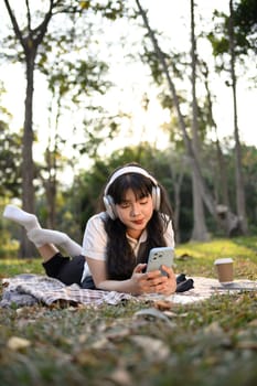 Portrait of relaxed young woman listening to music and using mobile phone on grass.