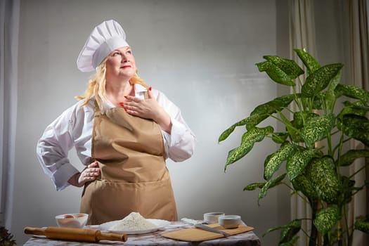 A fat funny female cook in a hat and apron poses in the kitchen and takes selfie. Good cooking and body positive