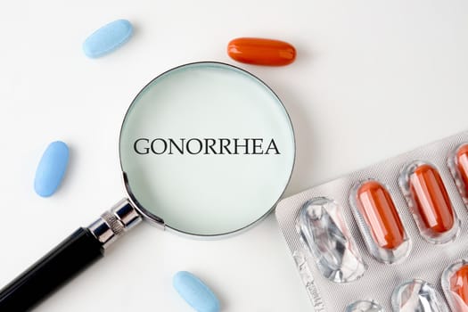 GONORRHEA word through a magnifying glass on a white background next to pills, medicines
