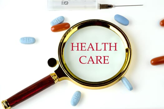 Medical concept. Health Care through a magnifying glass on a white background with pills and vitamins lying next to it