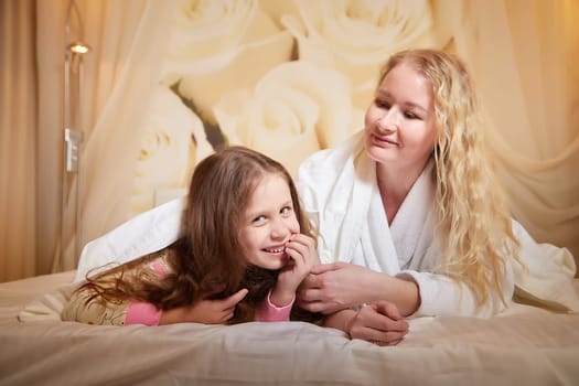 Mother and daughter happily relax and fun together on bed in bedroom. The concept of tenderness between mom and girl