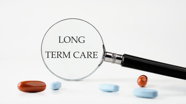 Medical concept. LONG TERM CARE text on a white background through a magnifying glass