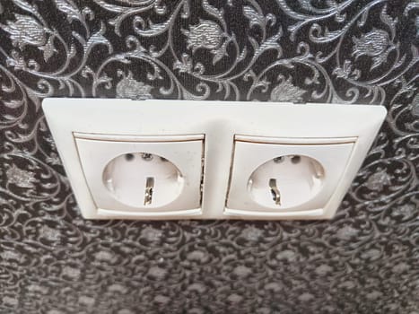 Two white European power outlets mounted on an ornate wall. European Dual Socket on a Patterned Wall