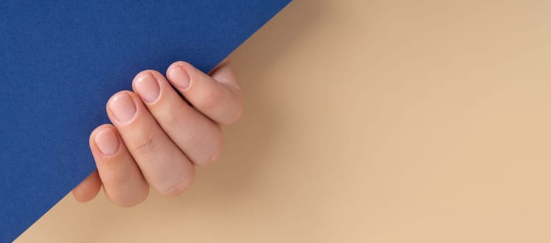 Woman manicured hands, stylish beige nails. Closeup of manicured nails of female hand in blue sweater in blue background. Mock up template copy space Winter or autumn style of nail design concept. Beauty treatment.