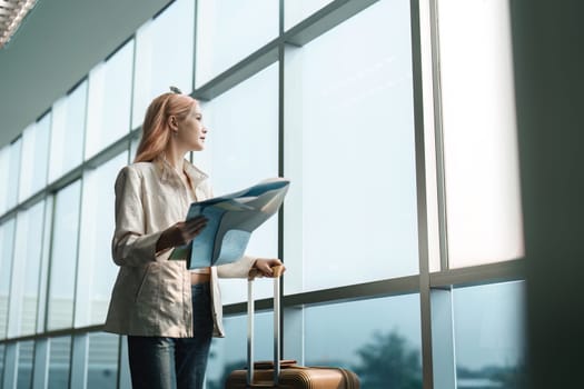 Happy young woman asian is stand in airport near suitcase and reading map.