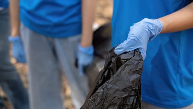 A group of Asian volunteers collects trash in plastic bags and cleaning areas in the forest to preserve the natural ecosystem..