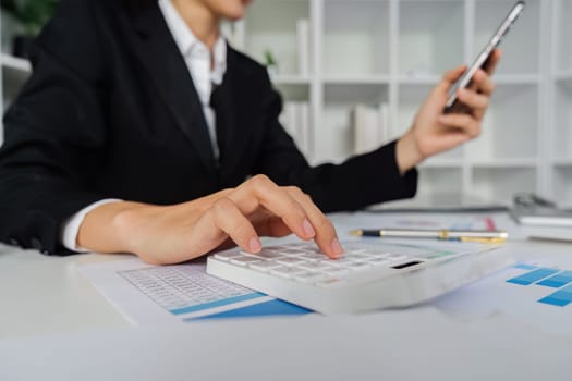 Businesswoman using a calculator to calculate numbers on a company's financial documents, she is analyzing historical financial data to plan how to grow the company. Financial concept.