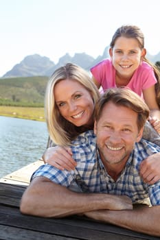 Smile, lake and portrait of family in nature for summer vacation, weekend trip and bonding together. Man, woman and relax with daughter outdoors for happiness, adventure and tourism travel in Europe.