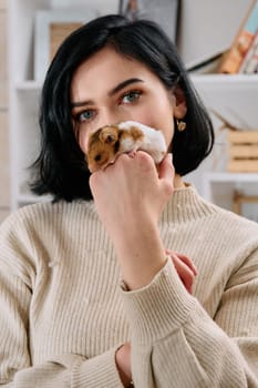 A black-haired woman enjoys a cozy day at home with her pet mouse, the two of them sharing a playful moment in the warm light of the living room.