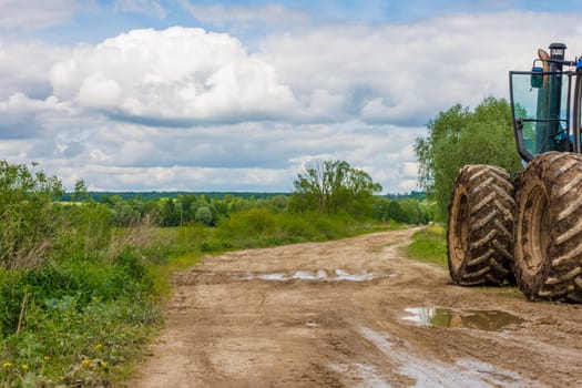 Tractor with large wheels on the edge of a dirt road at summer day with cloudy sky, copy space composition