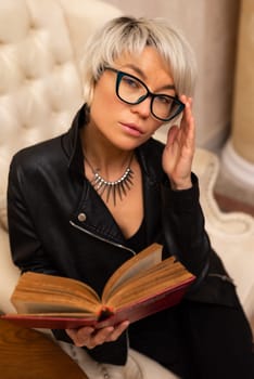 Portrait of an adult beautiful girl with glasses and short hair, holding a book in her hand in room