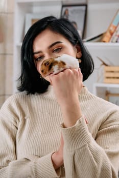 A black-haired woman enjoys a cozy day at home with her pet mouse, the two of them sharing a playful moment in the warm light of the living room.