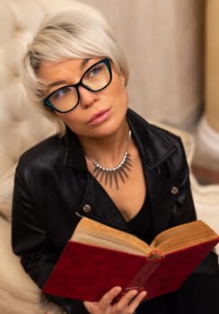 Portrait of an adult beautiful girl with glasses and short hair, holding a book in her hand in room