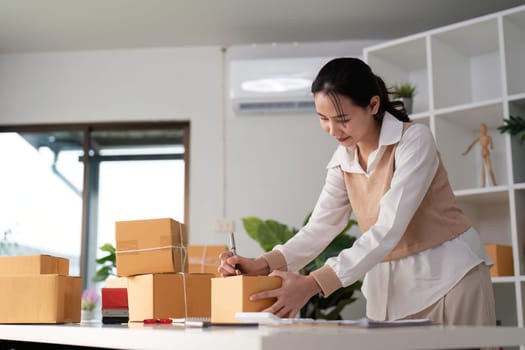 Woman asian is writing a list of customer on paper before shipping to them, she runs an ecommerce business on websites and social media. Concept of selling products online.