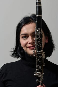 A talented brunette musician showcases her artistry as she gracefully holds and plays the clarinet against a pristine white background