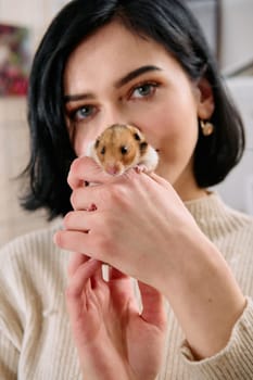 A black-haired woman enjoys a cozy day at home with her pet mouse, the two of them sharing a playful moment in the warm light of the living room.