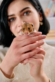 A black-haired woman enjoys a cozy day at home with her pet mouse, the two of them sharing a playful moment in the warm light of the living room.