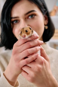 A black-haired woman enjoys a cozy day at home with her pet mouse, the two of them sharing a playful moment in the warm light of the living room.