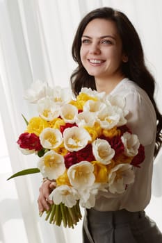 Beautiful woman in the white shirt with spring flowers tulips in hands. Women's Day