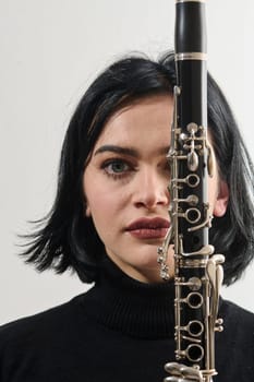 A talented brunette musician showcases her artistry as she gracefully holds and plays the clarinet against a pristine white background