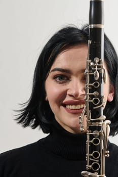 A talented brunette musician showcases her artistry as she gracefully holds and plays the clarinet against a pristine white background