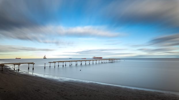 Captured long exposure photo of a calm sea and drifting clouds above a vintage pier.