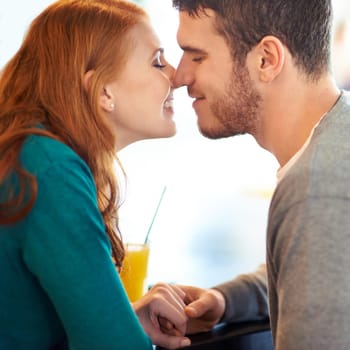 Couple, date and kiss with love, coffee shop or restaurant with happiness together. Man, woman and romance for relationship, care and smile for flirting on break for relax or bonding in cafe.