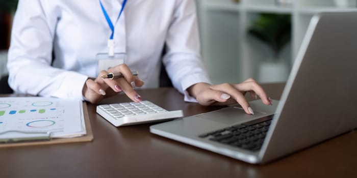 Finance concept. Close up businesswoman hold a graph pen and writing report, and memo, and analyzing business documents with a laptop computer.