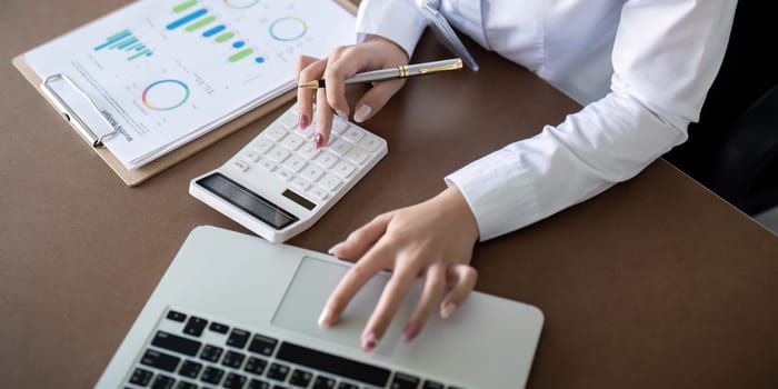 Finance concept. Close up businesswoman hold a graph pen and writing report, and memo, and analyzing business documents with a laptop computer.