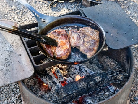 Steaks cooked on cast iron pan sear on a campfire grill