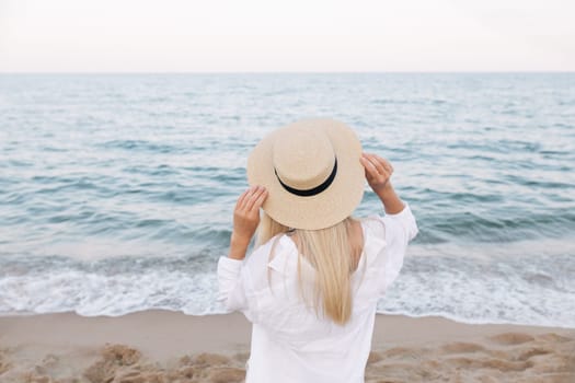 Pretty slim tanned blonde stylish woman in a straw hat posing on a paradise tropical beach.