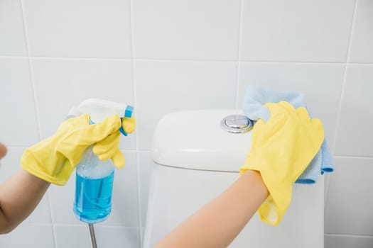 Maid in yellow gloves meticulously cleans the toilet seat in restroom using cloth. Her focus on purity and hygiene embodies the housekeeper dedication to bathroom care. Housekeeper healthcare concept
