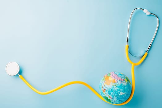 World Health Day. Yellow doctor stethoscope and world globe isolated on pastel blue background with copy space for text, Save world day, Green Earth Environment, Healthcare and medical concept