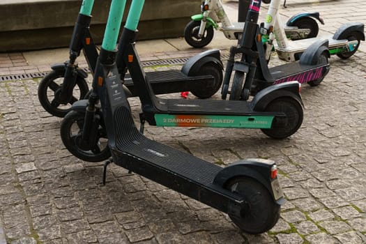 Warsaw, Poland - August 6, 2023: A group of parked electric scooters available for rent, with one scooter lying on its side on a cobblestone sidewalk.
