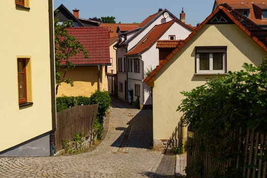 German city. A narrow cobblestone street lined with traditional houses leads to the distance.