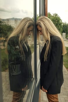 A woman stands near a glass window and looks into the glass.