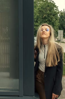 A woman wearing a black jacket is leaning against a glass door outdoors.