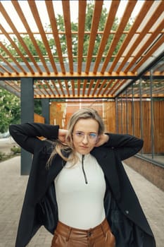 A woman wearing a white top and brown pants standing casually outdoors.