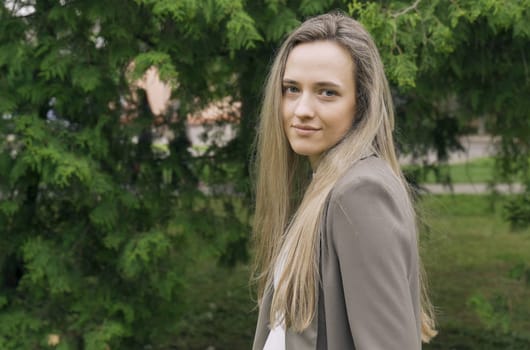 A woman standing in front of a tall tree, looking towards the camera.