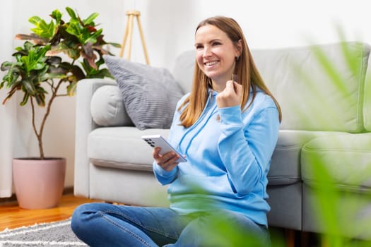 Smiling woman in blue sweater sitting on the floor using phone