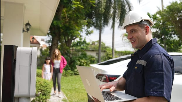 Qualified technician working on home EV charging station installation, making troubleshooting and configuration setup on charging system with laptop for EV at home. Synchronos