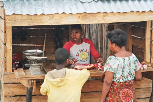 Ranohira, Madagascar - April 29, 2019:  Unknown Malagasy woman and boy buying raw meat from vendor at street stall. Food is usually bought on street, where it's left all day long and hygiene is low.