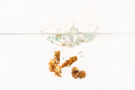 Walnut kernels dropped into water aquarium tank, high speed photo, white background