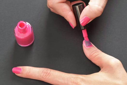 Applying pink nail polish - closeup photo of woman hands, little brush and fingernails on gray / black background