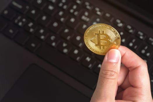 Woman hand holding golden coloured bitcoin coin over black laptop keyboard