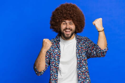 Happy cheerful Caucasian man celebrating success victory, winning birthday, lottery jackpot goal achievement play casino game good positive news triumph. Stylish guy isolated on blue studio background