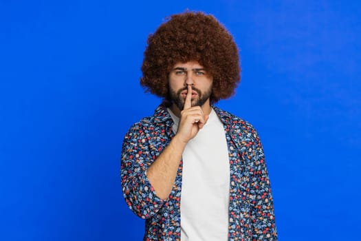 Shh be quiet please. Caucasian man presses index finger to lips makes silence gesture sign do not tells secret, stop talk gossip, confidential privacy. Stylish guy on blue background. Copy-space