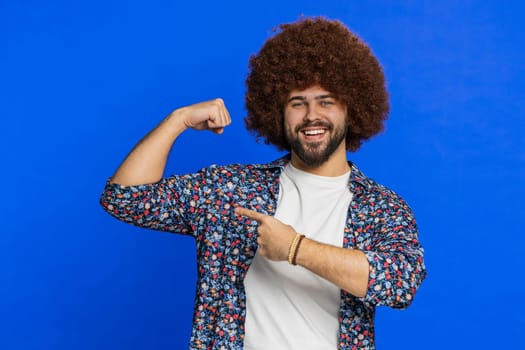 I am strong and independent. Man with Afro hairstyle wig showing biceps and looking confident, feeling power strength to fight for rights, energy to gain success win. Guy isolated on blue background