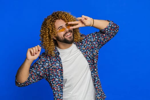 Caucasian stylish man wearing sunglasses charming smile celebrating success victory winning good positive news triumph success dancing. People emotions. Guy isolated on blue background. Copy-space
