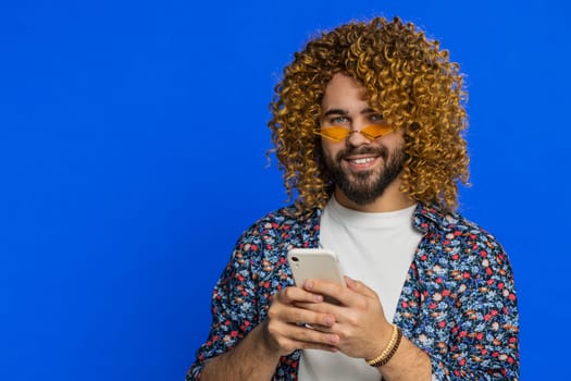 Man use smartphone typing post on web, browsing searching, addiction of social networks, showing positive application game feedback, recommends WIFI cellular connection on blue background. Copy-space